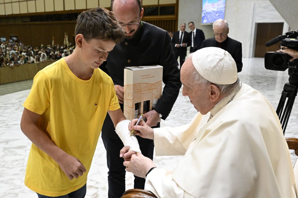 Pope Francis autographs the cast of a boy during his general audience in the Paul VI hall at the Vatican Aug. 31, 2022. 